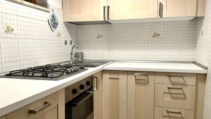 A kitchen with white tiled backsplash, wooden cabinets, a gas stove, and a stainless steel sink. - M397 - Marcelli, delightful three-room apartment 200m from the sea (Marcelli)