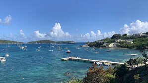 Un port de plaisance situé sur la côte, avec différents bateaux amarrés, une jetée et des bâtiments construits sur une colline.