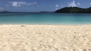 Une plage à l’eau turquoise et limpide, avec un rivage sablonneux et une île visible au loin.