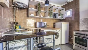Une cuisine compacte équipée d’un lave-vaisselle encastré, d’une cuisinière et d’un four à micro-ondes. On y trouve des étagères au-dessus du plan de travail et une plante suspendue.