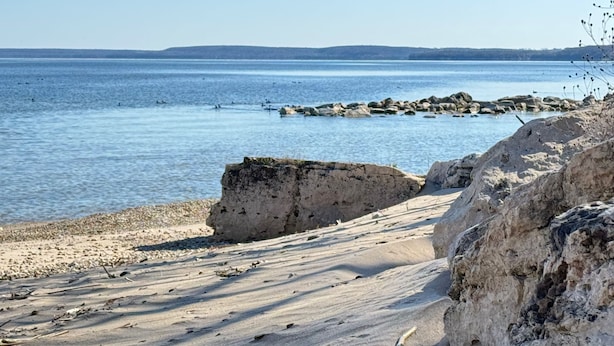 Eine Küstenlandschaft mit felsiger Küste, ruhiger See und fernen Hügeln.