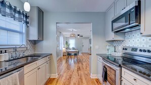 Una cocina moderna con suelo de madera, armarios blancos, microondas integrado y una barra para café.