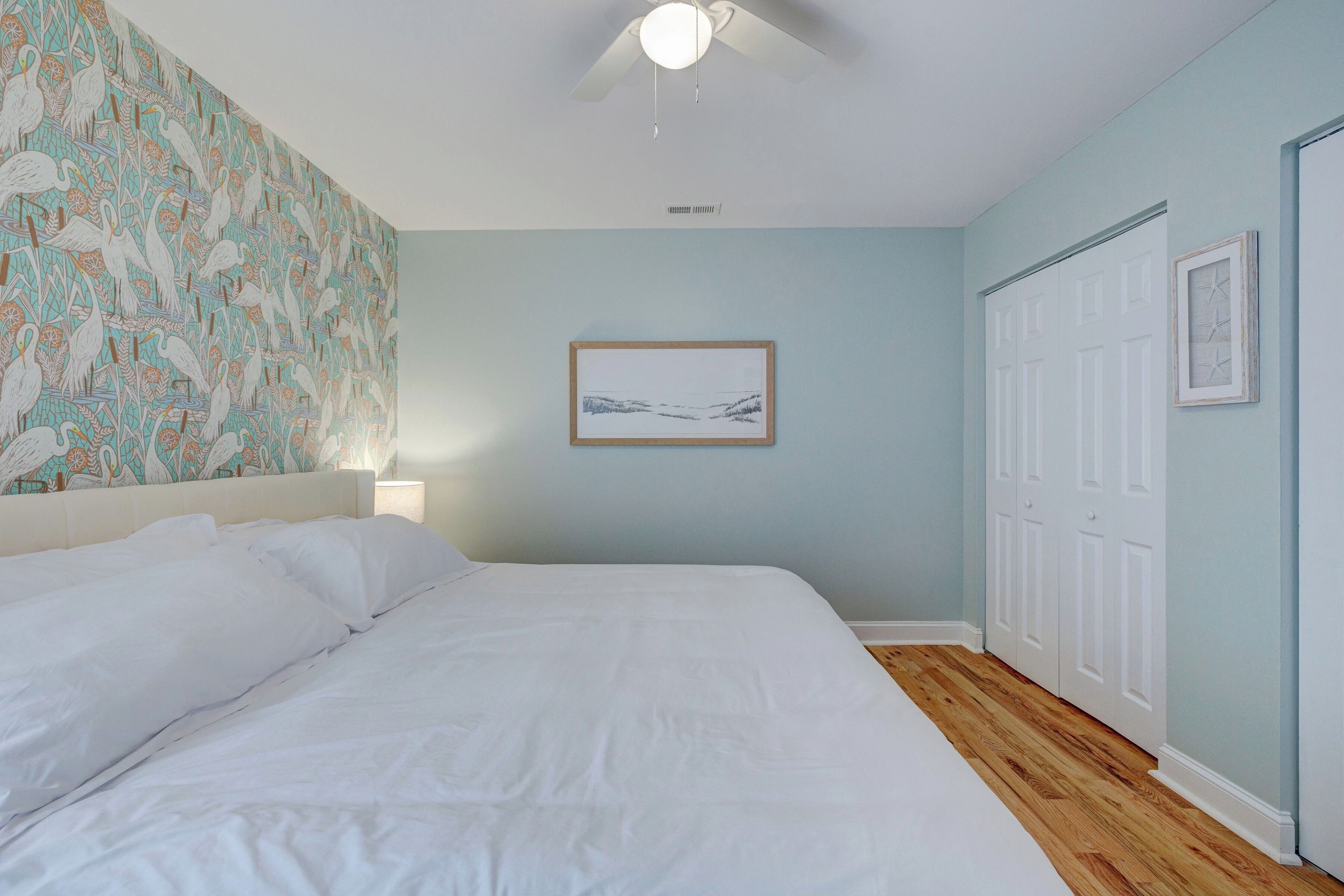Una camera da letto con un letto, una ventola a soffitto, un quadro appeso al muro e una porta.