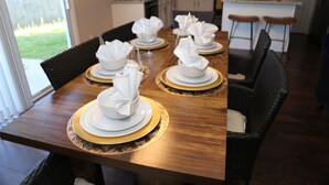 Une table à manger dressée avec de l’argenterie blanche, des assiettes décoratives dorées et des serviettes pliées.