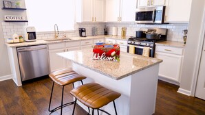 Une cuisine moderne avec des meubles blancs, un îlot en granit, des appareils en acier inoxydable et un coin café.