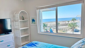 A bedroom with a large window offering a view of the beach and ocean.