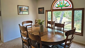 Comedor con mesa y sillas de madera, ventilador de techo y ventana de vidrio emplomado con vistas al exterior.