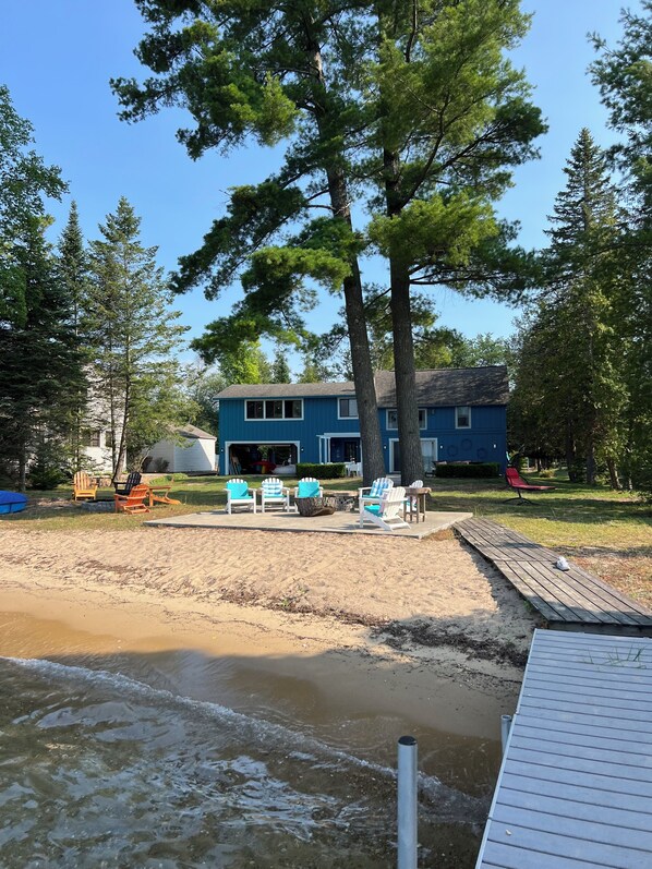 A beach house with a blue exterior, surrounded by trees and a sandy beach. - Torch lake house (Rapid City)