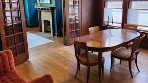 Un coin repas avec une table et des chaises en bois, un fauteuil rouge recouvert de tissu et un ventilateur de plafond.