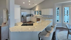 A modern kitchen with a central island, white cabinetry, and a large window providing natural light.