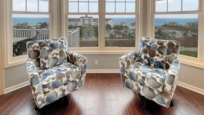 A room with two armchairs facing a large bay window overlooking a coastal view.