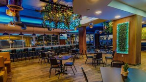Un restaurant moderne avec un plancher en bois, des chaises et des tables noires. On y trouve des luminaires suspendus et un mur végétal.