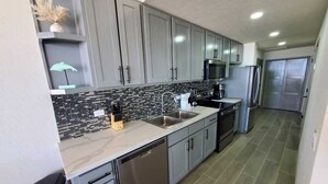 A modern kitchen with grey cabinets, a black and white backsplash, stainless steel appliances, and a tiled floor.