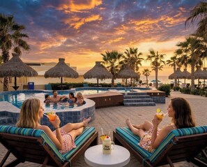 Un espace aménagé au bord de la piscine, avec des chaises longues, un jacuzzi et une vue sur l’océan au coucher du soleil.