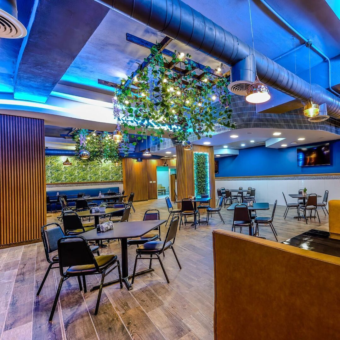 Een modern restaurant met verschillende eetgedeeltes, houten vloeren en hangende groene planten.