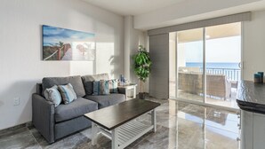 Una sala de estar moderna con un sofá gris, una mesa de centro de madera y un amplio ventanal con vistas al océano.