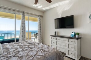 A bedroom with a bed, a TV, a dresser, and a balcony with a view of the ocean.