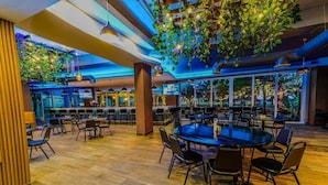 Un vaste espace de restauration intérieur, doté de nombreuses tables et chaises, d’un plancher en bois et d’un plafond agrémenté de plantes suspendues et de luminaires.