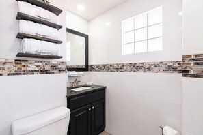 A modern bathroom with white tiles, a marble backsplash, a black vanity, and a toilet. - 2 bedroom 2 bath, C30901 (Puerto Peñasco)