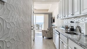 Cozinha moderna com armários brancos, bancada de mármore e vista para o exterior.