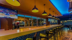 Uma área de bar com um balcão comprido, várias luminárias pendentes e banquetas.