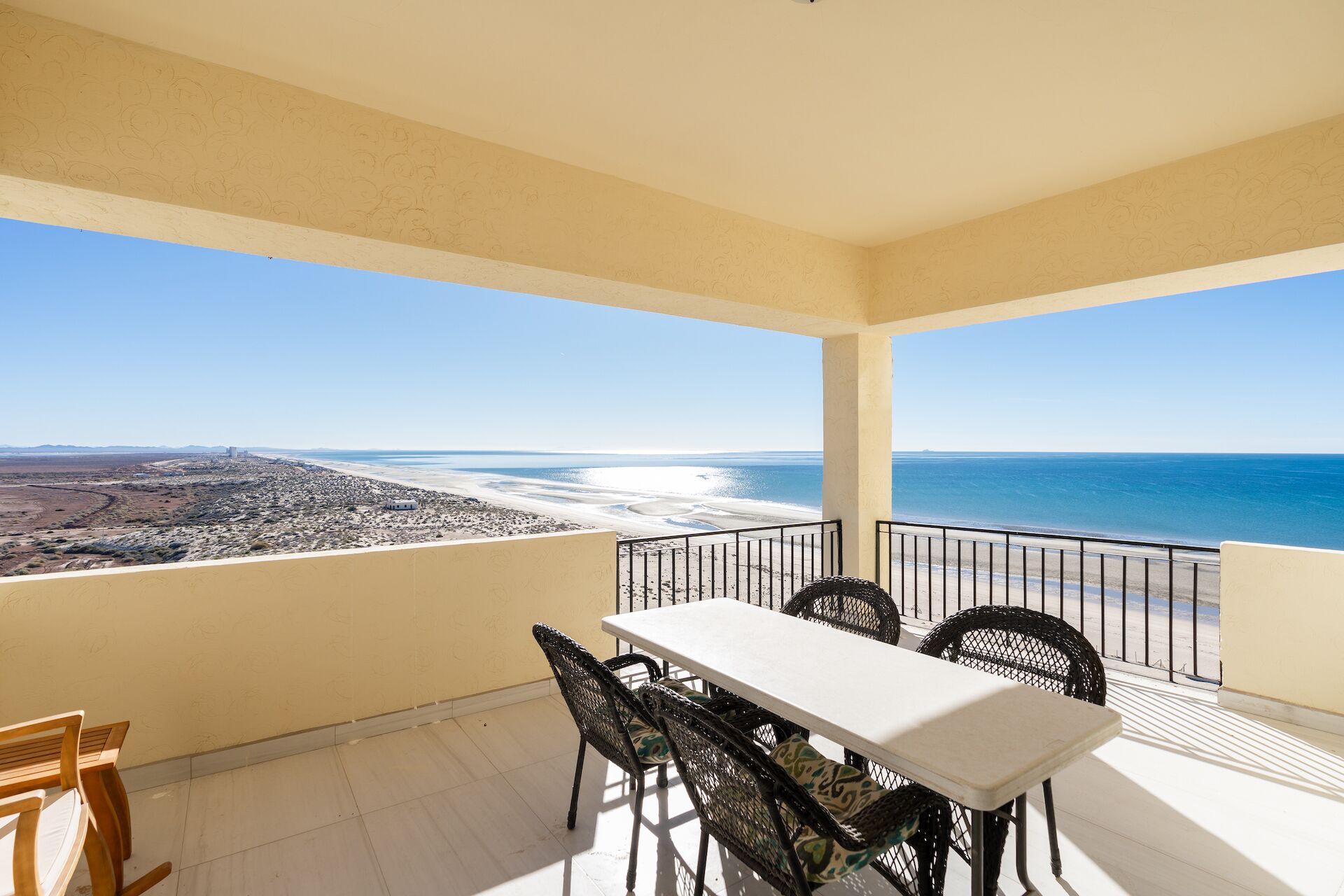 A balcony with a table and chairs, offering a view of the beach and ocean.