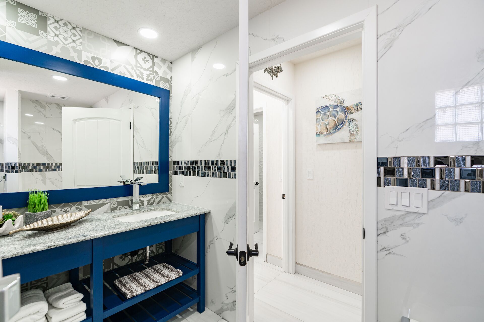 A modern bathroom with a marble backsplash, a blue vanity, and a glass shower enclosure.
