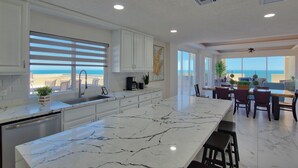 A modern kitchen with a large island, white cabinetry, and a view of the ocean.