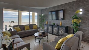 Ein modernes Wohnzimmer mit einem grauen Sofa, gelben Kissen, einem Couchtisch und einem an einer strukturierten Wand befestigten Fernseher.