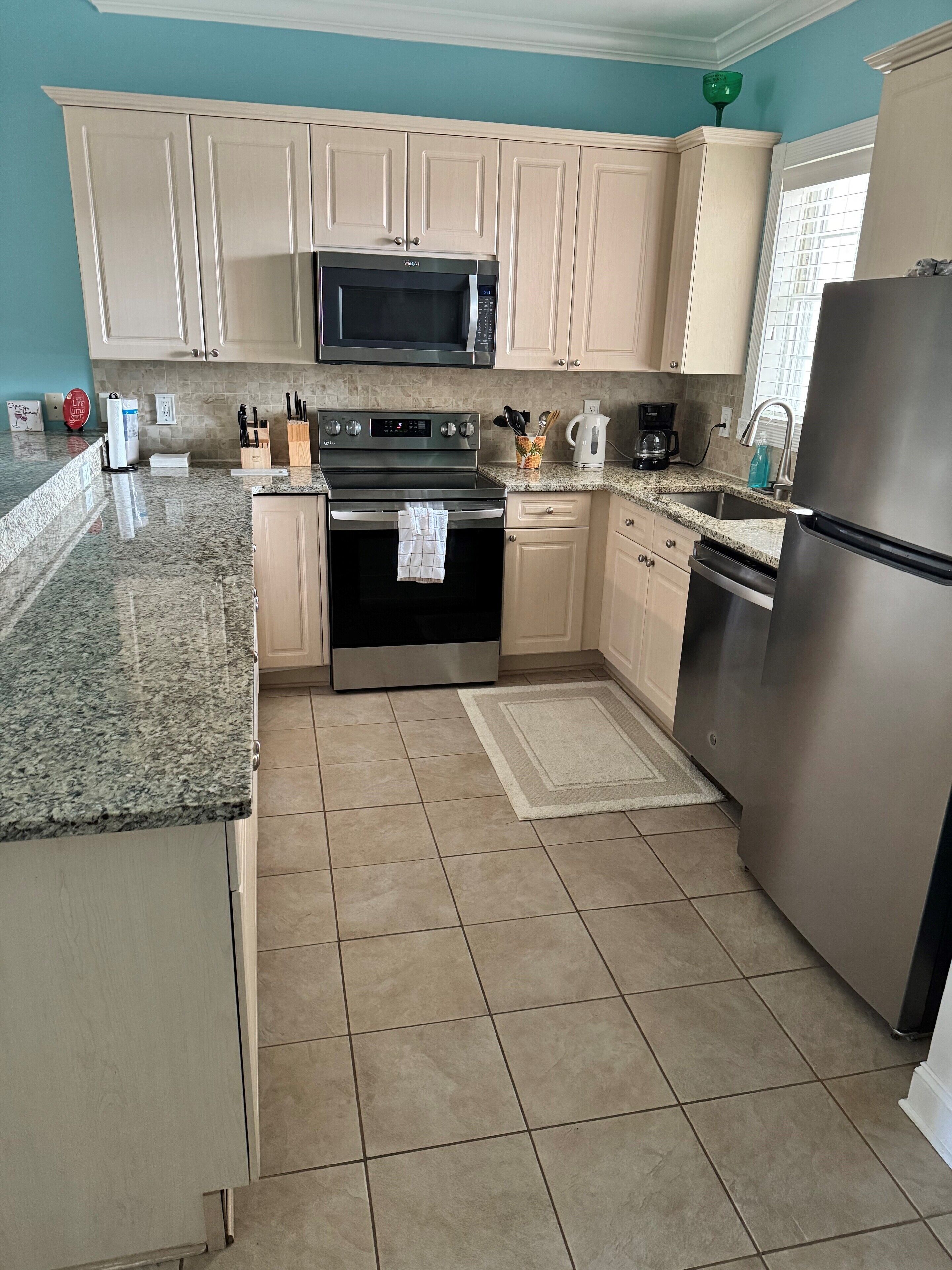 A kitchen with beige cabinets, a stainless steel refrigerator, a microwave, an oven, and a granite countertop.