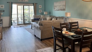 A spacious living room with a large sectional sofa, a dining table with chairs, a ceiling fan, and a chandelier.