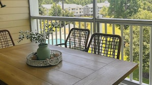 A wooden table with a vase of flowers and a woven basket, set on a balcony with a view of a residential area and trees.
