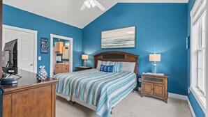 A bedroom with a bed, bedside tables, a desk, a ceiling fan, and a window.