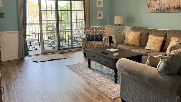 A living room with a dark wood floor, a grey sofa, a coffee table, and a ceiling fan.
