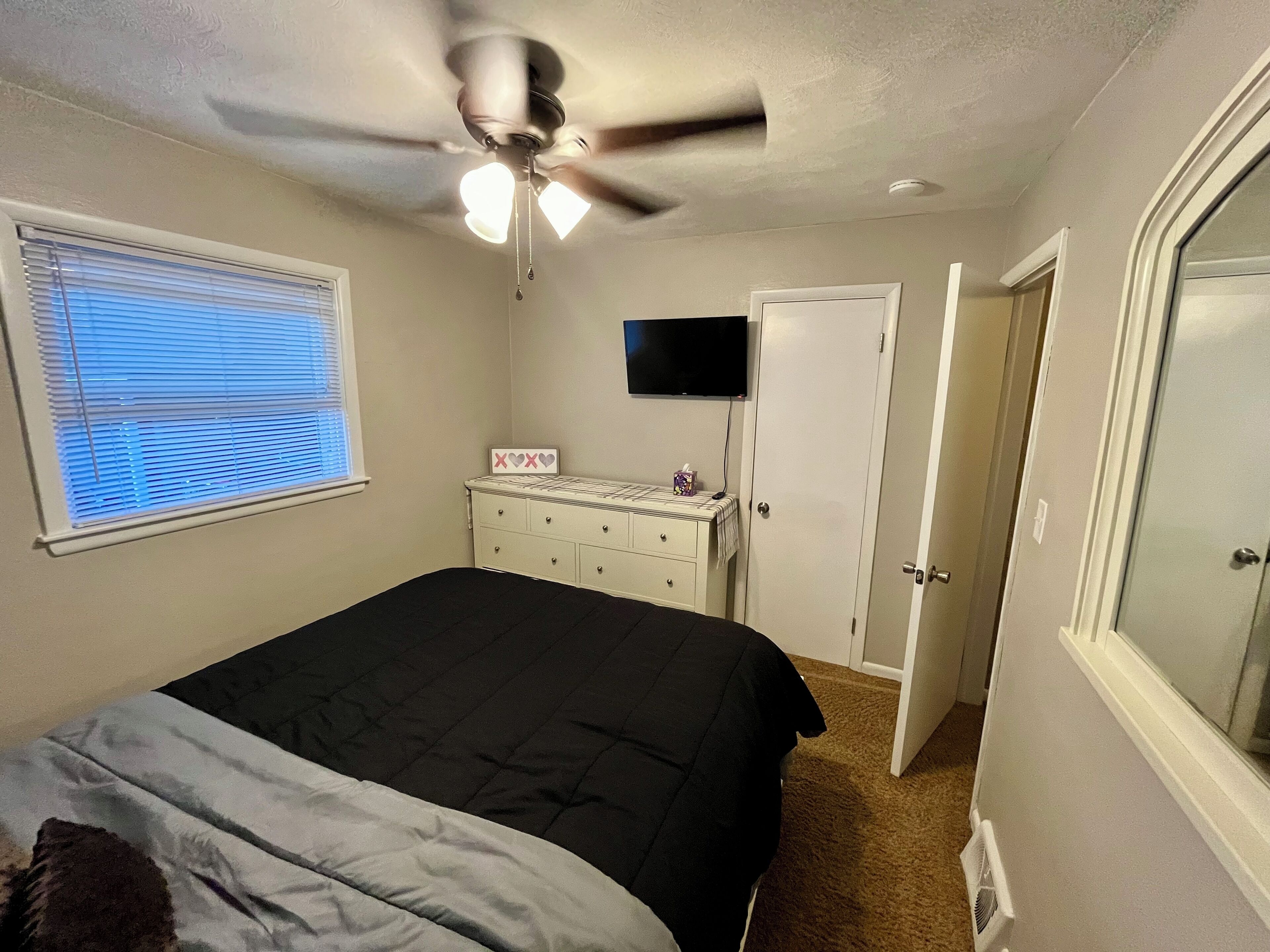 A bedroom with a bed, a dresser, a ceiling fan, a TV, and a window with blinds.