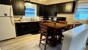 Una cocina con armarios oscuros, un refrigerador blanco, una mesa de comedor de madera con sillas, un microondas y un lavamanos.