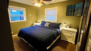 Un dormitorio con cama, mesitas de noche, ventilador de techo y ventana.