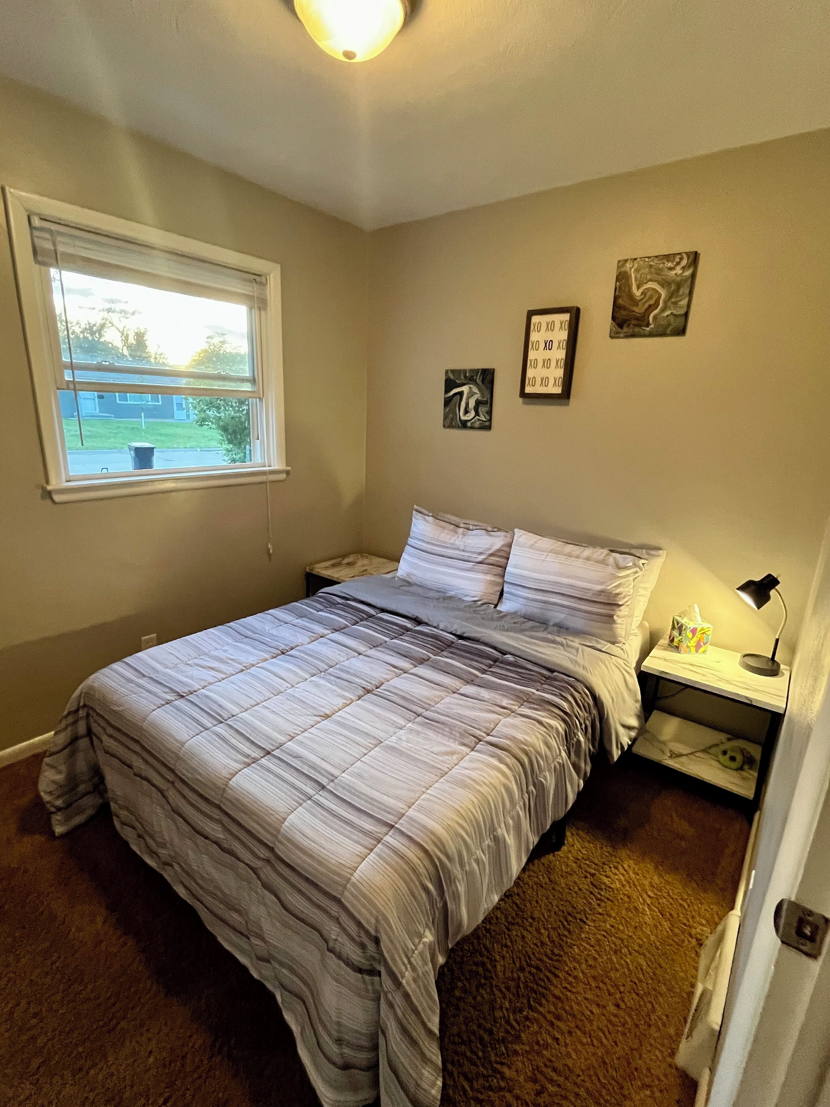 Un dormitorio con cama, mesita de noche, ventana y decoración en la pared.
