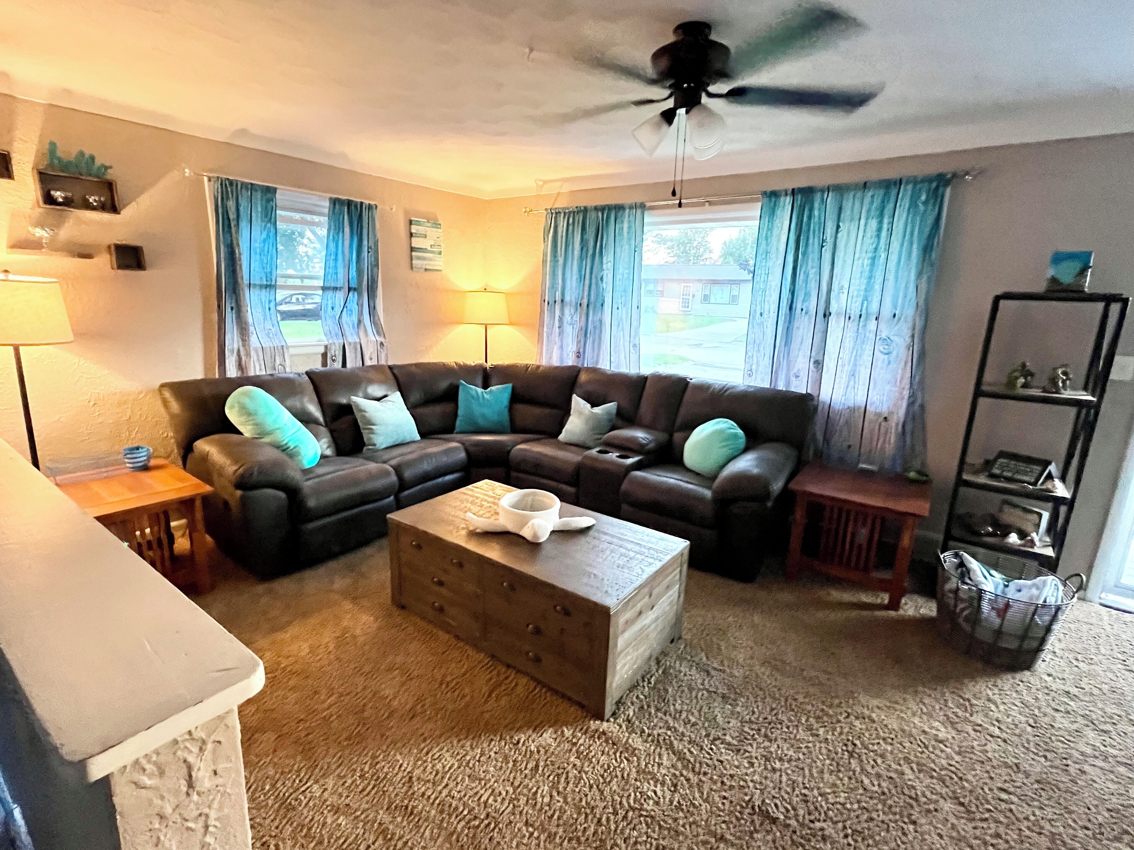 Ein Wohnzimmer mit Ecksofa, Couchtisch, Deckenventilator und Bücherregal.