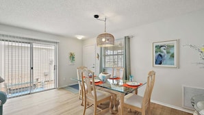 A dining area with a glass table, wooden chairs, and a hanging light fixture.