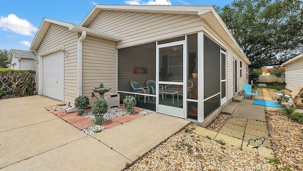 A single-story house with a covered patio, a garage, and a small garden area with potted plants and a pathway.
