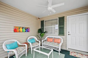 A porch with wicker furniture, a ceiling fan, and a door with a welcome mat.