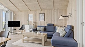 A modern living room with a wooden ceiling, a blue sofa set, a coffee table, and a television. - 3 bedroom awesome home in Faaborg (Faaborg)