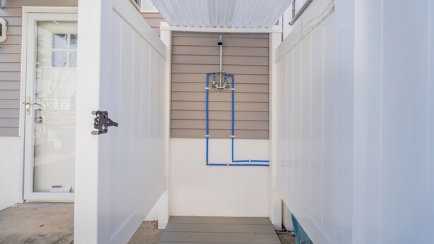 Un pasillo estrecho con una puerta a la izquierda y una zona de ducha con tuberías a la derecha.
