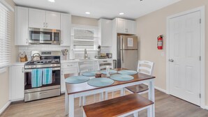 Una cocina compacta con armarios blancos, microondas, estufa y refrigerador. Hay una mesa de comedor con individuales y sillas.