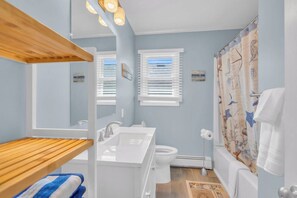 A bathroom with a wooden shelf, a sink, a toilet, and a shower curtain with a nautical theme. - High Speed Wifi | Washer/Dryer | Linens+ Towels (Seaside Heights)