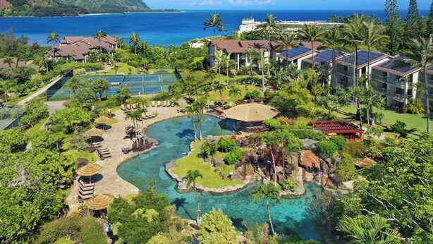 A resort with a large pool area, multiple buildings, and a view of the ocean. - Hanalei Bay Resort 52012 - Newly updated, Bay views, Private walk to beach & AC! (Princeville)