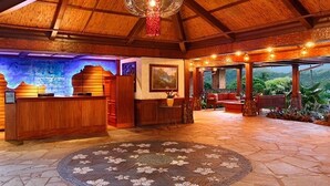 A reception area with a wooden reception desk, a round rug, and a seating area with a view of the outdoors. - Hanalei Bay Resort 52012 - Newly updated, Bay views, Private walk to beach & AC! (Princeville)