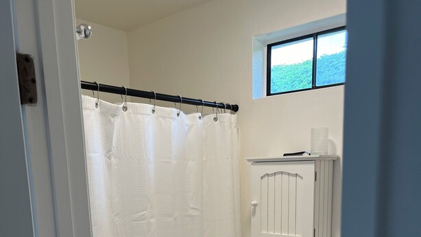 Un baño con inodoro blanco, cortina de ducha y una ventana sobre el inodoro.