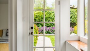 Puerta blanca con un panel de vidrio que da a un jardín con diversas plantas y flores.